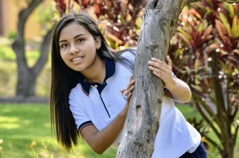 Alumna de High School junto a un árbol del jardín